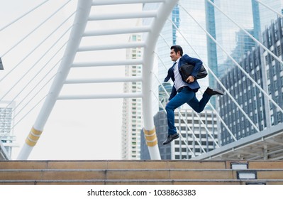 Asian Businessman In Formal Wear Holding Briefcase While Running And Jump In The City On A Background Of Building. Late For Work Concept