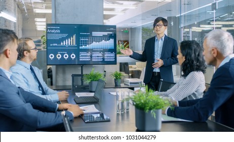 Asian Businessman Gives Report/ Presentation to His Business Colleagues, Pointing at the Results Showing Statistics, Pie Charts and Company's Growth On Wall TV Screen. - Shutterstock ID 1031044279