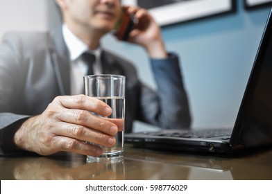 Asian Businessman In Grey Suit Holding Glass Of Dink Water While Working With Using Mobile Phone And Laptop Computer. Health Care.