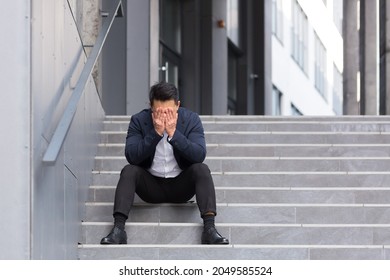 Asian businessman has a severe headache sitting on the stairs near the office - Powered by Shutterstock