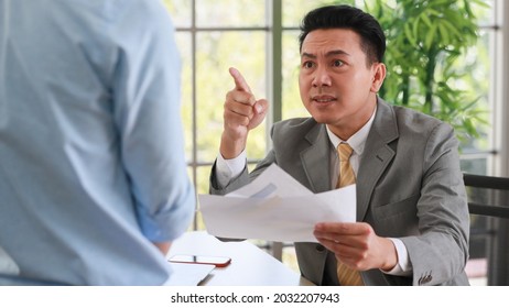 Asian Businessman Manager In Suit Holding Paperwork And Point Finger To Young Employee With Anger And Serious Gesture Look Like He Comments As Disagree Or Unacceptable For His Project Work.