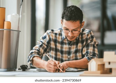 Asian businessman person with glasses examining architectural blueprints next to model house, engineer architect working on new house project and apartment. - Powered by Shutterstock