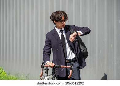 Asian businessman pushing his bicycle and looking on watch in the morning preparing to ride his bicycle to work. Eco tranportation
