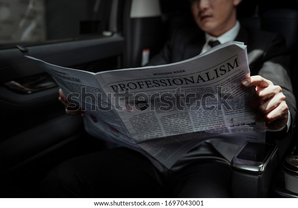 Asian businessman reading\
newspaper in a car, gaining insight into the latest stock market\
report, 
