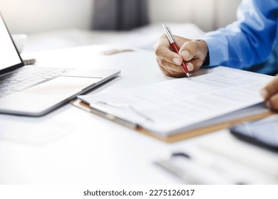 Asian businessman reviewing document reports at office workplace with computer laptop. legal expert, professional lawyer reading and checking financial documents or insurance contract - Shutterstock ID 2275126017