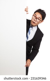 Asian businessman shock peeking from behind blank banner  isolated on white background