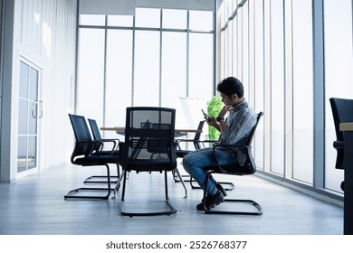 Asian businessman sitting in modern office building using smartphone and laptop on desk in office. - Powered by Shutterstock