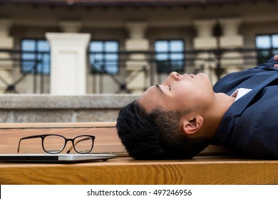 Asian Businessman Sleeping On Bench Outside. Concept Of Working Too Much And Not Getting Enough Sleep Is Bad For You.