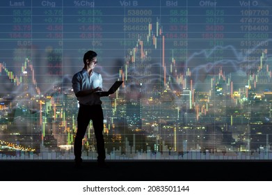 Asian Businessman Standing And Using The Smart Mobile Phone Showing The Stock Market Chart Over The Cityscape Background At Night Time, Business  Technology And Trading Concept