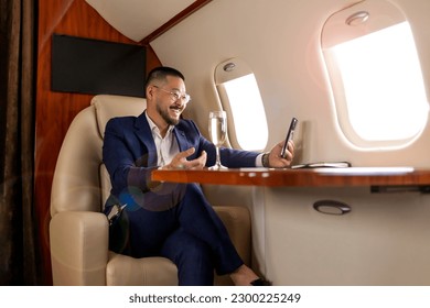 asian businessman in suit and glasses with glass of champagne flies in luxury jet and uses smartphone, korean entrepreneur films himself on the phone and communicates via video call - Powered by Shutterstock