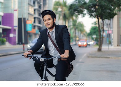 Asian businessman in a suit is riding a bicycle on the city streets for his morning commute to work. Eco Transportation Concept.