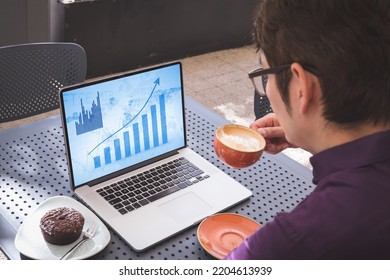 Asian Businessman At Table In Cafe Using Laptop With Blue Graphs On Screen. Business Communication, Flexible Working, Data And Digital Interface Concept.