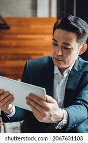 Asian Businessman Talking On Video Call Meeting In A Cafe. 
Serious Business Man In Blue Suit Attending On Online Web Conference On A Digital Tablet.