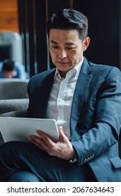 Asian Businessman Talking On Video Call Meeting In A Cafe. 
Serious Business Man In Blue Suit Attending On Online Web Conference On A Digital Tablet.