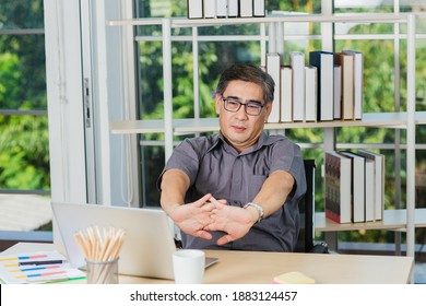 Asian Businessman Tired Overworked He Stretch Oneself On The Desk. Senior Man With Eyeglasses Break Stretching His Arms On Table At His Working Place