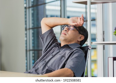 Asian businessman tired overworked he relaxing with closed eyes and hands behind his head on the desk. senior man with eyeglasses lying asleep on table at his working place