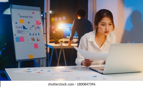 Asian businessman turn off computer and say goodbye his colleague who still working when he get off work after finish working overtime in small modern home office night. - Shutterstock ID 1800847396