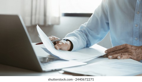 Asian businessman using computer laptop working and reviewing document reports at office workplace. legal expert, professional lawyer reading and checking financial documents or insurance contract - Powered by Shutterstock