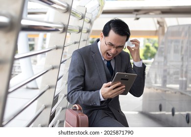 Asian Businessman Using Mobile Phone And Angry Outside Of Office In Urban City. Asian Man Holding Smartphone For Business Work.