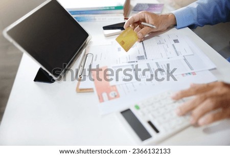 Asian businessman using tablet work on desk holding credit card and checking receipt, documents related to business operations calculate expenses paid via credit card before finalizing the account