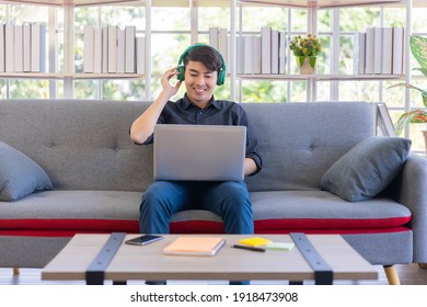 An Asian businessman wear headset while having video conference. An Asian man enjoy music and entertainment with headset sitting on sofa in living room
