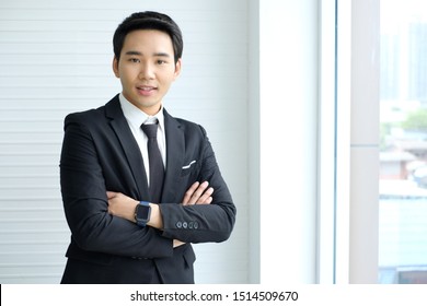 Asian businessman is wearing a black suit ,smiling and standing with arms crossed,white office,young businessman,finance,Intelligent and confident people,Successful leader/Management/finance