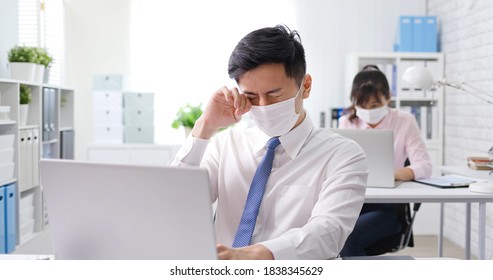 asian businessman wearing face mask feel eyes fatigue when he work in the office and his colleague is behind him  - Powered by Shutterstock