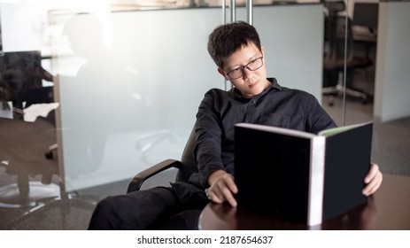 Asian Businessman Wearing Glasses Reading Book In Public Library. Education Research And Self Improvement With Printed Media. World Book Day Concept