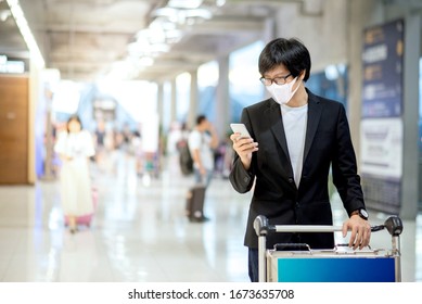 Asian businessman wearing mask using smartphone walking with airport trolley in airport terminal. Coronavirus (COVID-19) outbreak prevention. Health awareness for pandemic protection - Powered by Shutterstock