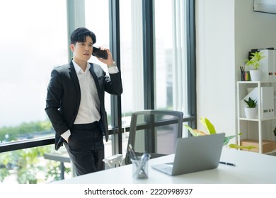 Asian Businessman Wearing Suit Holding Mobile Phone Standing In Workstation Office