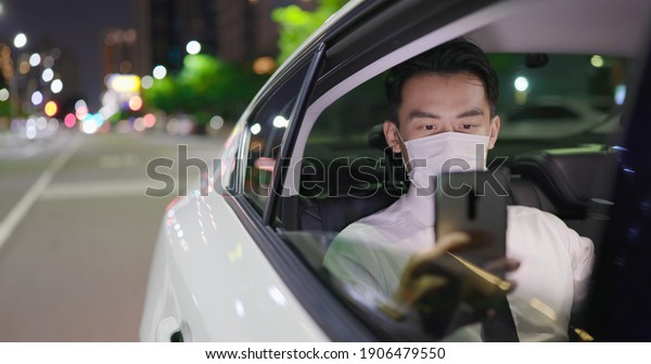 asian businessman wears face mask to avoid\
infectious diseases coronavirus and uses smart phone while\
commuting by taxi