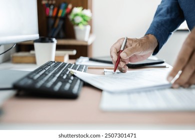 Asian businessman working with desktop PC holding pen checking business contract and document report before sign, asian man working at home meeting online via desktop PC