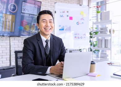 Asian Businessman Working On Laptop Computer At Modern Office. Male Professional Pay Attention To Computer At Office Workplace. Portrait Of Positive Business Man Looking At Laptop Screen Indoors.