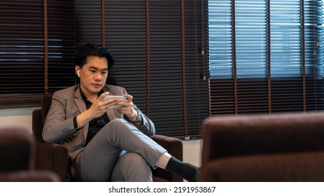 Asian Businessman Working On Mobile Phone At Airport Private Lounge While Waiting For Boarding In Airport Terminal. Airline Service Business, Airplane Transportation And Holiday Vacation Concept