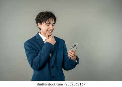 Asian businessman working and using mobile phone in isolated background. Attractive young employee man feeling happy and cheerful while chatting on digital smartphone device equipment in grey studio. - Powered by Shutterstock