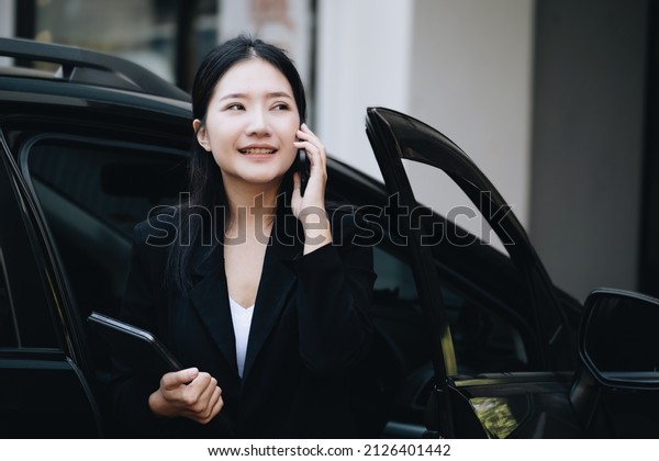 Asian businessmen, business owners, company\
presidents or female employees talking on the phone and holding a\
tablet are getting out of the car to attend a business plan meeting\
at the meeting