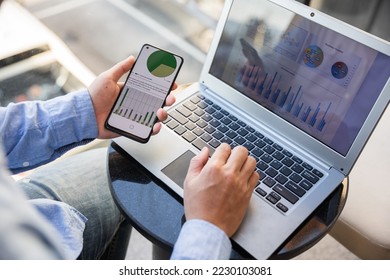 Asian businessmen use equipment for business. Holding a smartphone that works with laptops and mobile phones, showing statistics and software apps. - Shutterstock ID 2230103081