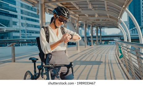 Asian businesswoman with backpack bicycle smiling look smartwatch in city street go to work at office. Sports girl use her watch app for fitness tracking. Commute to work, Business commuter in city.