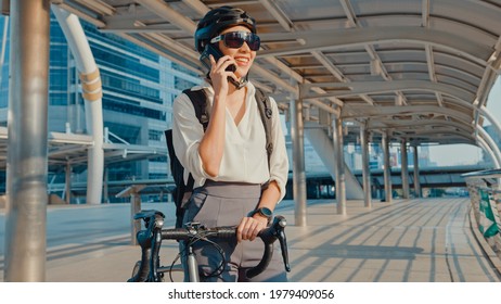 Asian businesswoman with backpack call mobilephone talk smiling in city street go to work at office. Sports girl use her phone for working business. Commute to work by bike, Business commuter in city. - Powered by Shutterstock