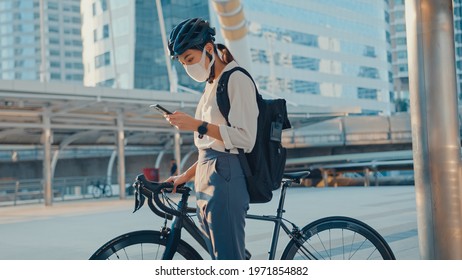 Asian businesswoman carry backpack wear anti virus protection mask take bicycle walk and check phone in city street go to work at office. commute to work, Business commuter for covid-19 concept. - Powered by Shutterstock