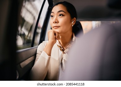 Asian Businesswoman Commuting To Work On Backseat Of A Car And Thinking While Looking Through The Window. 