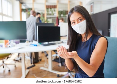 Asian businesswoman with face mask for Covid-19 disinfecting hands in open plan office - Powered by Shutterstock