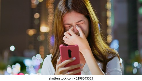 asian businesswoman feel eye tired and neck pain while using smartphone on the blurred street background in the evening