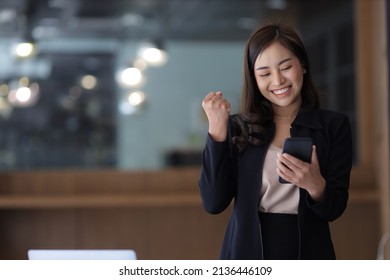 Asian Businesswoman In Formal Suit In Office Happy And Cheerful During Using Smartphone And Working. Asian Female Employees Express The Excitement Of Success And Bonuses.