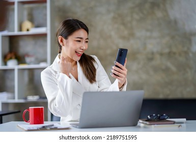 Asian Businesswoman In A Formal Suit In The Office Happy And Cheerful During Using Smartphone And Working. Asian Female Employees Express The Excitement Of Success And Bonuses.