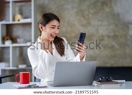 Asian businesswoman in a formal suit in the office happy and cheerful during using smartphone and working. Asian female employees express the excitement of success and bonuses.