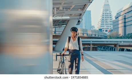 Asian businesswoman go to work at office walk and smile wear backpack look around take bicycle on street around building on a city street. Bike commuting, Commute on bike, Business commuter concept.