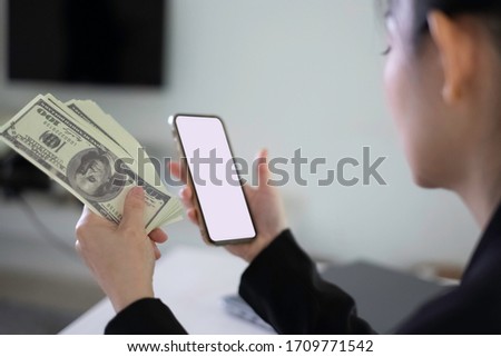 Asian businesswoman holding dollar banknotes & smartphone. Asian businesswoman holding dollar cash for stock investment & making payment by mobile banking. E-commerce & mobile banking concept. 