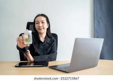 Asian businesswoman is holding a plant in a bottle while sitting at her desk in her office - Powered by Shutterstock