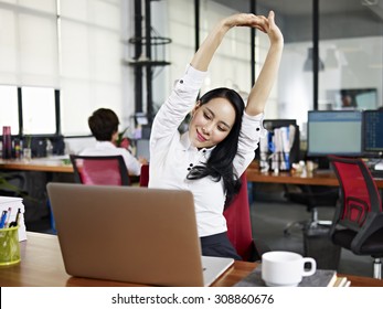 asian businesswoman looking at work on laptop computer with satisfaction and stretching arms in the air.